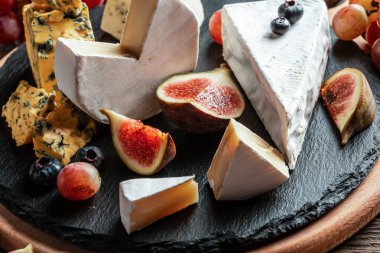 Çeşitli peynir çeşitleri, geleneksel Fransız parçaları, İtalyan ve İspanyol manchego peyniri üzümlü ve incirli ahşap masada servis edilmiş..