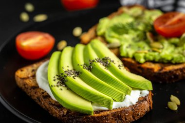 Kahvaltıda sağlıklı avokado tostları ya da öğle yemeğinde çavdar ekmeği, krem peynir, roka, dilimlenmiş avokado, balkabağı, kenevir ve susam tohumu, tuz ve biber. Vejetaryen gıda konsepti. Temiz yemek. Üst görünüm.