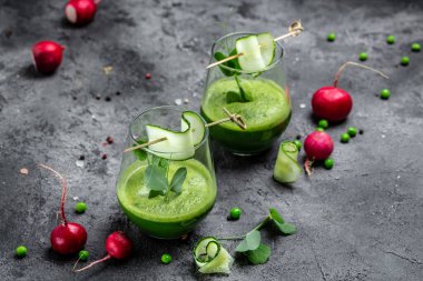 Beton arka planda bir bardakta salatalık yeşili smoothie tazeliyorum. Detox smoothie, taze bezelye, salatalık, turp, ıspanak ve limon. dikey görüntü. en üstteki görünüm.