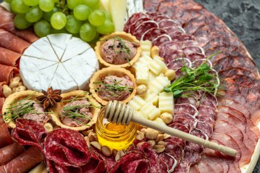 Antipasto tabağı Grissini ekmek çubukları, prosciutto, jambon, üzüm, jambon, kurutulmuş et, sucuklu salam, fuet, börek ve bal. Tahtada keçi peyniri var.