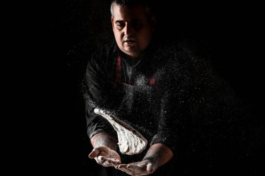 Un dağılmış halde pizza hamuru uçurmak. Siyah üzerine bir un bulutunun dondurucu hareketiyle. Hamur yoğuran elleri pişir. Boşluğu kopyala.