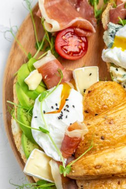 İspanyol kahvaltısı, kruvasan tostu ya da haşlanmış yumurta, jambon, mavi peynir, avokado, mikrocin ve vişneli domates, bir fincan kahve, yemek tarifi geçmişi. dikey resim.