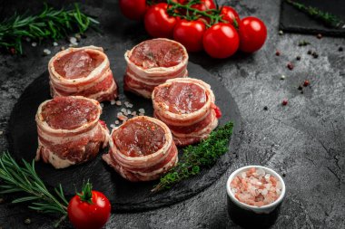 Çiğ et fileto mignon bifteği, metel tepside, biber ve tuzlu, fileminyon. Domuz pastırmasına sarılı sığır filetosu biftekleri ve koyu arkaplanda kekik. en üstteki görünüm.