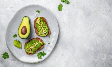 Kahvaltıda sağlıklı avokado tostları ya da öğle yemeğinde çavdar ekmeği, dilimlenmiş avokado, balkabağı tohumu, tuz ve biber. Vejetaryen yemeği. Bitki temelli diyet. Temiz yemek. Üst Manzara. Boşluğu kopyala,