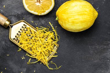 Akdeniz tariflerine tat katmak için limon kabuğu soyuyorlar. Siyah arkaplanda rende kabuk ve limon tadı, metin için yer, üst görünüm.