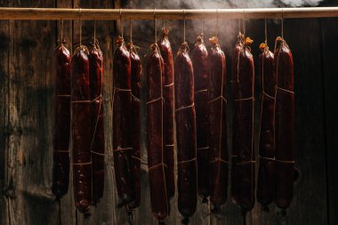 Sigara içme işlemi dumanlı bir dolapta asılı duruyor. Duman bulutları yükselir ve sallanan sosisleri sarar. Uzun pankart biçimi,