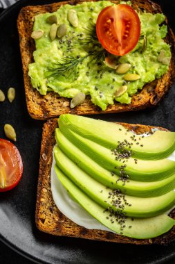 Kahvaltıda sağlıklı avokado tostları ya da öğle yemeğinde çavdar ekmeği, dilimlenmiş avokado, roka, balkabağı ve susam tohumu, tuz ve biber. Vejetaryen yemeği. Bitki temelli diyet. Temiz yemek. Üst görünüm.