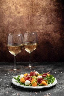 Akdeniz salatası jambon, mozzarella ve yeşil fesleğen yaprakları ve kavun kavunu beyaz masada, geleneksel İspanyol ve İtalyan aperatifi toptan Grissini ile servis edilir..