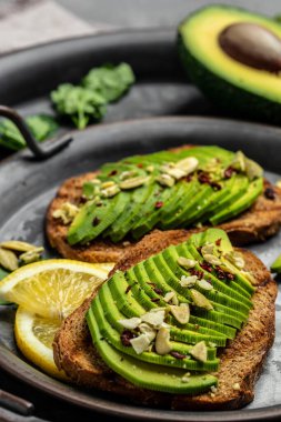 Sağlıklı avokado tostları ve çavdar ekmeği. Kahvaltıda ya da öğle yemeğinde dilimlenmiş avokado. Vejetaryen yemeği. Vejetaryen menüsü. Yemek tarifi. dikey görüntü. Üst Manzara. metin için yer.