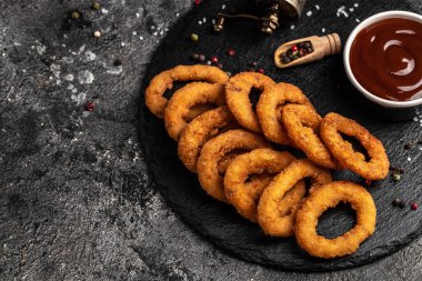 Kızarmış soğan halkaları yuvarlak siyah taş tepside servis edilir, Amerikan sağlıksız kalori yemeği. Lezzetli bir bar tarzı, aperatif, restoran menüsü, üst manzara.,