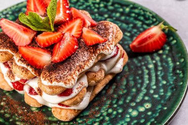 Çilekli tiramisu ve mascarpone. Yaz tatlısı, nane yapraklarıyla süslenmiş çilekli klasik tiramisu..