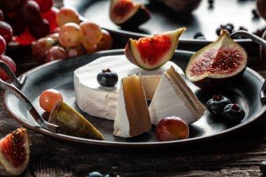 Çeşitli peynir çeşitleri, geleneksel Fransız parçaları, İtalyan ve İspanyol manchego peyniri üzümlü ve incirli ahşap masada servis edilmiş..