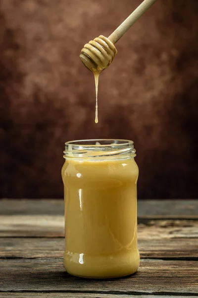 甜蜂蜜放在玻璃瓶中 勺子放在木制背景上 蜜蜂生产新鲜的 健康的蜂蜜 亲爱的背景 养蜂业概念 — 图库照片