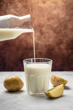 Bardakta vejetaryen patates sütü ve çiğ patates. Alternatif bitkisel süt. Donmuş hareket sıçrama damlaları. dikey görüntü. metin için yer.