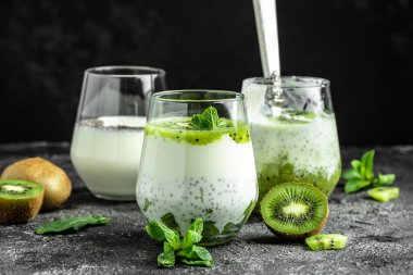 Sağlıklı kahvaltılık chia pudingi. Koyu masada cam kavanozlarda kivi var. Temiz yemek, diyet, vejetaryen yemek konsepti. pankart, menü, tarif, metin için yer.
