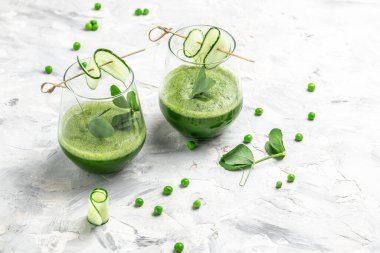 Beton arka planda bir bardakta salatalık yeşili smoothie tazeliyorum. Detox smoothie, taze bezelye, salatalık, turp, ıspanak ve limon. dikey görüntü. en üstteki görünüm.