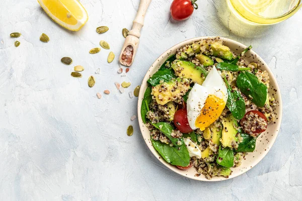 Keto diet plate quinoa, avocado, egg, tomatoes, spinach and sunflower seeds on light background. Healthy food, ketogenic diet, diet lunch concept, place for text, top view.