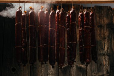 Sigara içme işlemi dumanlı bir dolapta asılı duruyor. Duman bulutları yükselir ve sallanan sosisleri sarar..