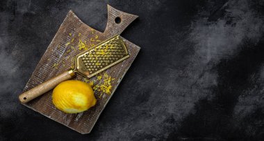 Akdeniz tariflerine tat katmak için limon kabuğu soyuyorlar. Siyah zemin üzerinde rende kabuğu ve limon tadı, uzun pankart biçimi. en üstteki görünüm.