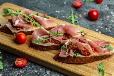 Kurutulmuş domatesler, prosciutto ve roka ile ahşap bir tahtanın üzerinde. Lezzetli kahvaltı..