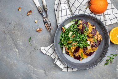 Arugula, pancar ve portakal salatası, çatallı ceviz, sos ve gri arka planda baharat, vitamin salatası. Düzgün beslenme. metin için yer, üst görünüm.