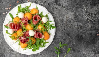 Prosciutto ve fesleğenli taze kavun. Antipasti, geleneksel İspanyolca ve İtalyan aperatifleri. Koyu taş masadaki üst manzara, uzun pankart biçimi. en üstteki görünüm.