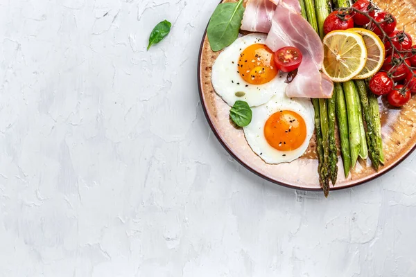 Lezzetli bir kahvaltı. Yeşil kuşkonmaz, pastırma, jambon ve vişneli domatesli yumurta. Sağlıklı dengeli yiyecekler. Üst görünüm, yukarıda, afiş.