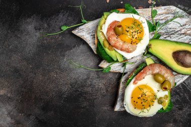 Açık sandiviçli sandviç, yağda yumurta, ıspanak, avokado, siyah arka planda karides, ketogenik kahvaltı. Süper yiyecek konsepti. Sağlıklı, temiz yemek. Üst görünüm.