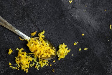 Akdeniz tariflerine tat katmak için limon kabuğu soyuyorlar. Siyah arkaplanda rende kabuk ve limon tadı, metin için yer, üst görünüm.