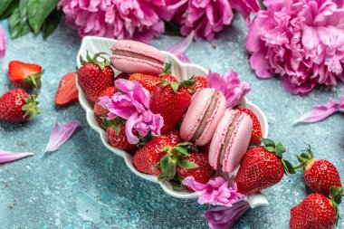 Pembe şakayık çiçeği ve makarna kurabiyeleri ve mavi arka planda tatlı çilek. Meyveli küçük Fransız pastaları. en üstteki görünüm.