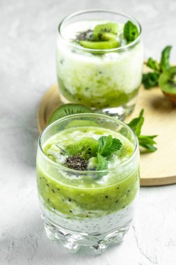 Sağlıklı kahvaltı pudingi, beyaz bir masada cam kavanozlarda kivi var. Temiz yemek, diyet, vejetaryen yemek konsepti. dikey resim.