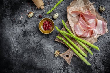 Kuşkonmaz ve pastırma koyu bir arka planda pişmeye hazır. Keto Paleo diyeti. afiş, menü, metin için tarif yeri, üst görünüm.