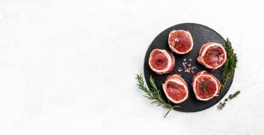 Çiğ et fileto mignon bifteği, metel tepside, biber ve tuzlu, fileminyon. Domuz pastırmasına sarılı sığır filetosu biftekleri ve arka planda kekik. Uzun afiş biçimi. en üstteki görünüm.