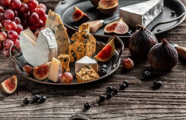 Çeşitli peynir çeşitleri, geleneksel Fransız parçaları, İtalyan ve İspanyol manchego peyniri üzümlü ve incirli ahşap masada servis edilmiş..