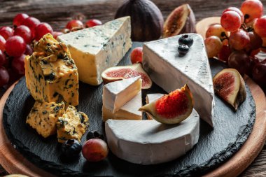 Çeşitli peynir çeşitleri, geleneksel Fransız parçaları, İtalyan ve İspanyol manchego peyniri üzümlü ve incirli ahşap masada servis edilmiş..