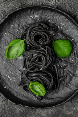 Mürekkep balığı mürekkebi ve yeşil fesleğen yapraklı siyah makarna. Kalamar mürekkepli, keçi buğdaylı makarna. Vejetaryen ya da glütensiz diyet. dikey görüntü. Üst Manzara. metin için yer.