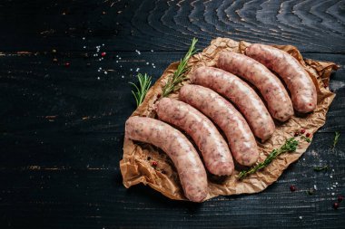 Çiğ melez kasaplar ahşap bir arka planda bitkilerle ve biberiyeyle kabuklu sosisler. Izgara için sosis. afiş, menü, metin için tarif yeri, üst görünüm.