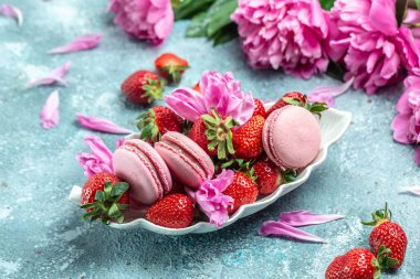 Pembe şakayık çiçeği ve makarna kurabiyeleri ve mavi arka planda tatlı çilek. Meyveli küçük Fransız pastaları. en üstteki görünüm.