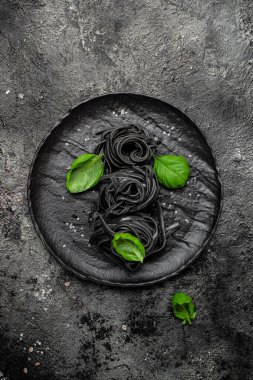 Mürekkep balığı mürekkebi ve yeşil fesleğen yapraklı siyah makarna. Kalamar mürekkepli, keçi buğdaylı makarna. Vejetaryen ya da glütensiz diyet. dikey görüntü. Üst Manzara. metin için yer.