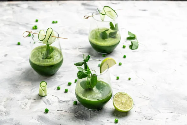 Beton arka planda bir bardakta salatalık yeşili smoothie tazeliyorum. Detox smoothie, taze bezelye, salatalık, turp, ıspanak ve limon. en üstteki görünüm.
