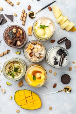 Cam kavanozda servis edilen lezzetli dondurma, İtalyan tatlı dondurması şam fıstığı, çikolata, karamel, kavun, mango, çikolatalı sandviç kurabiyeleri, dikey görüntü. en üstteki görünüm,