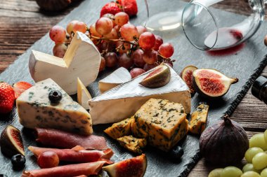 Çeşitli peynir çeşitleri, geleneksel Fransız parçaları, İtalyan ve İspanyol manchego peyniri üzümlü ve incirli ahşap masada servis edilmiş..