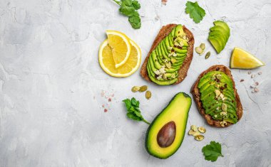 Kahvaltıda sağlıklı avokado tostları ya da öğle yemeğinde çavdar ekmeği, dilimlenmiş avokado, balkabağı tohumu, tuz ve biber. Vejetaryen yemeği. Bitki temelli diyet. Temiz yemek. Üst Manzara. Boşluğu kopyala,