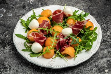Akdeniz salatası jambon, mozzarella ve yeşil fesleğen yaprakları ve kavun kavunu beyaz masada, geleneksel İspanyol ve İtalyan aperatifi toptan Grissini ile servis edilir..
