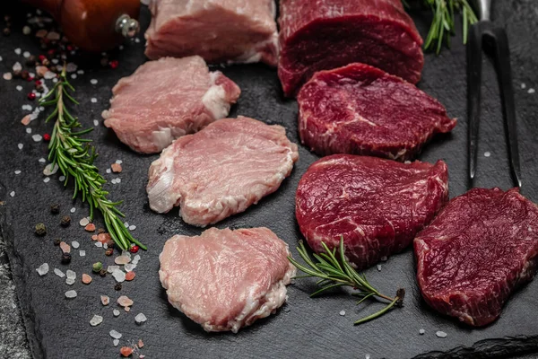Koyu arkaplanda farklı türde çiğ domuz eti ve sığır eti. Taze et, domuz eti ve sığır eti çeşitleri. Restoran menüsü, diyet, yemek kitabı tarifi üst görünümü.