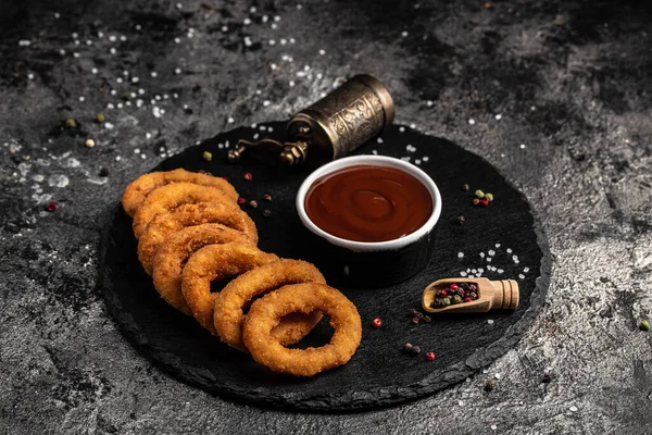 Kızarmış soğan halkaları yuvarlak siyah taş tepside servis edilir, Amerikan sağlıksız kalori yemeği. Lezzetli bir bar tarzı, aperatif, restoran menüsü, üst manzara.,