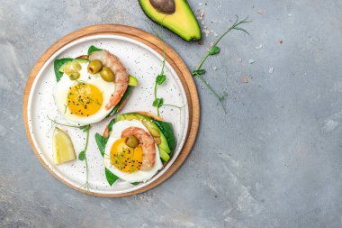 Tost ekmeği, yağda yumurta, ıspanak, avokado, gri arka planda karides, ketogenik kahvaltı. Süper yiyecek konsepti. Sağlıklı, temiz yemek. Üst görünüm.