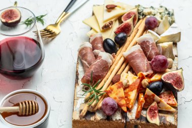 İtalyan atıştırmalıkları ve bardakta şarap olan aperatifler. Peynir, jambon, fındık, meyve, ekmek çubukları. Lezzetli dengeli gıda konsepti.