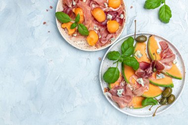 Prosciutto ve fesleğenli taze kavun. Antipasti, geleneksel İspanyolca ve İtalyan aperatifleri. Beyaz taş masadaki üst manzara, uzun pankart biçimi. en üstteki görünüm,