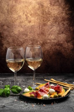 Prosciutto veya jamonlu Akdeniz salatası, mozzarella ve yeşil fesleğen yaprakları ve kavun kavunu koyu masada, geleneksel İspanyol ve İtalyan aperatifleri toptan Grissini ile servis edilir, üst görünüm.